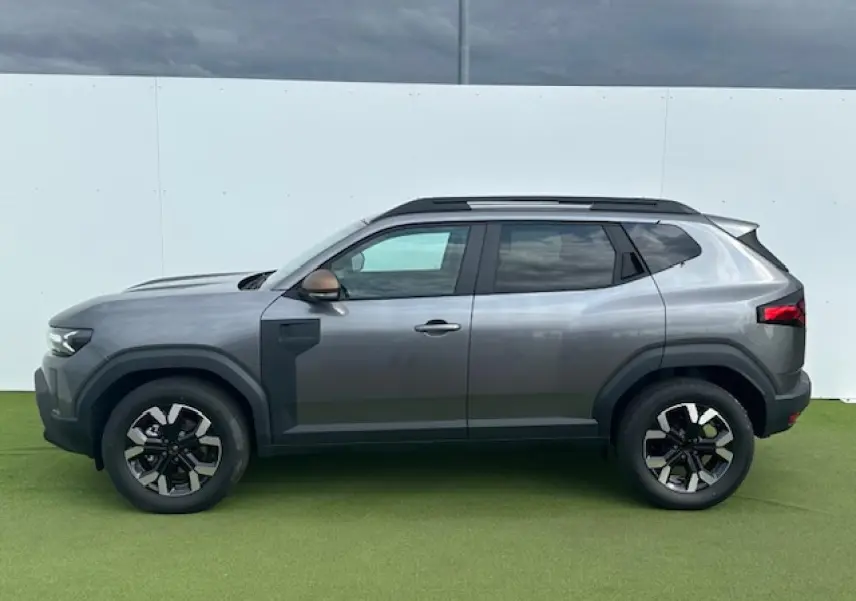 Profil côté gauche du Dacia Duster III gris schiste métallisé avec jantes alliage et barres de toit noires.