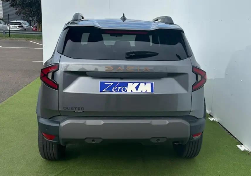 Vue arrière du Dacia Duster III gris schiste métal 2025 avec feux LED en forme de C et barres de toit noires.