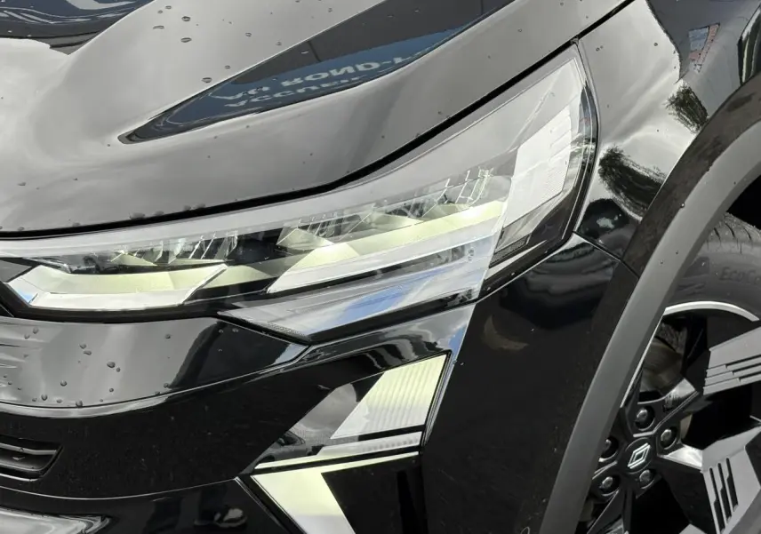 Gros plan sur le phare avant droit et la jante 18" noire du Renault SYMBIOZ noir étoile, finition E-Tech Full Hybrid.