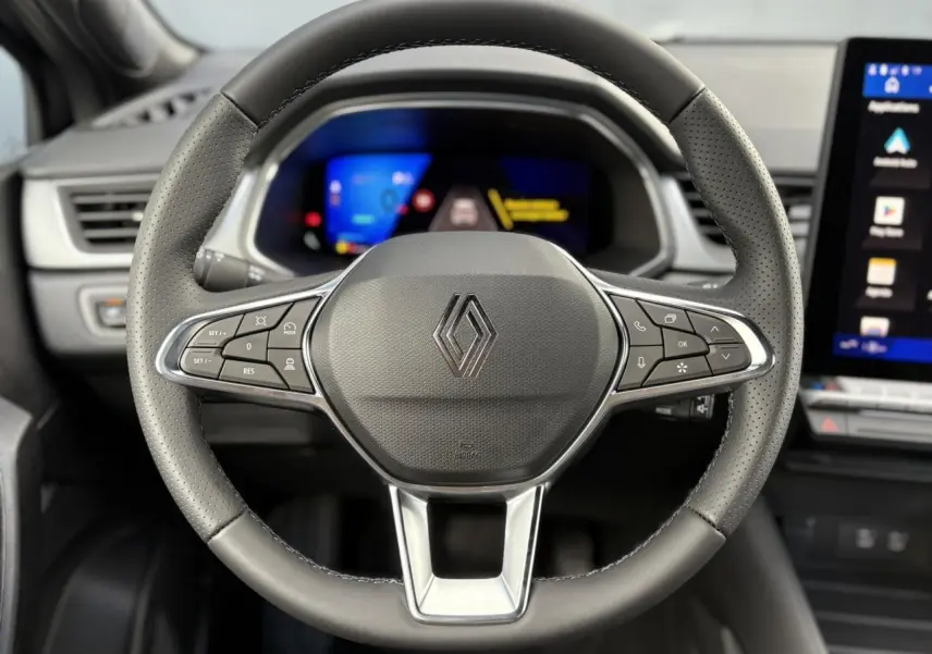 Volant en cuir noir avec commandes multifonctions et logo Renault, tableau de bord numérique flou en arrière-plan