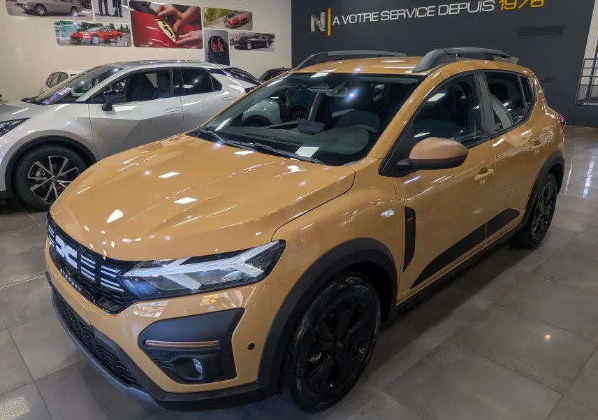 Vue 3/4 avant droite d'une Dacia Sandero Stepway beige Safari avec jantes noires et détails noirs contrastants.
