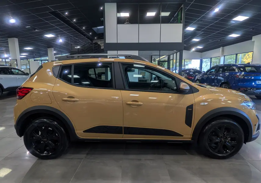 Vue de profil côté gauche d'une Dacia Sandero Stepway TCe 110 Beige Safari avec jantes noires et protections noires sur les bas de caisse.