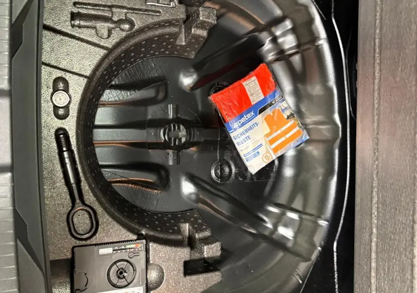 Coffre ouvert montrant le rangement noir du Volkswagen T-Roc 1.5 TSI 2025 avec kit de sécurité et espace pour roue de secours.