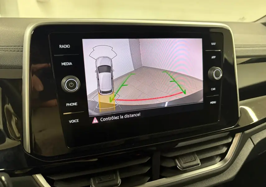 Écran central affichant la caméra de recul avec vue aérienne du Volkswagen T-Roc blanc pur en stationnement.