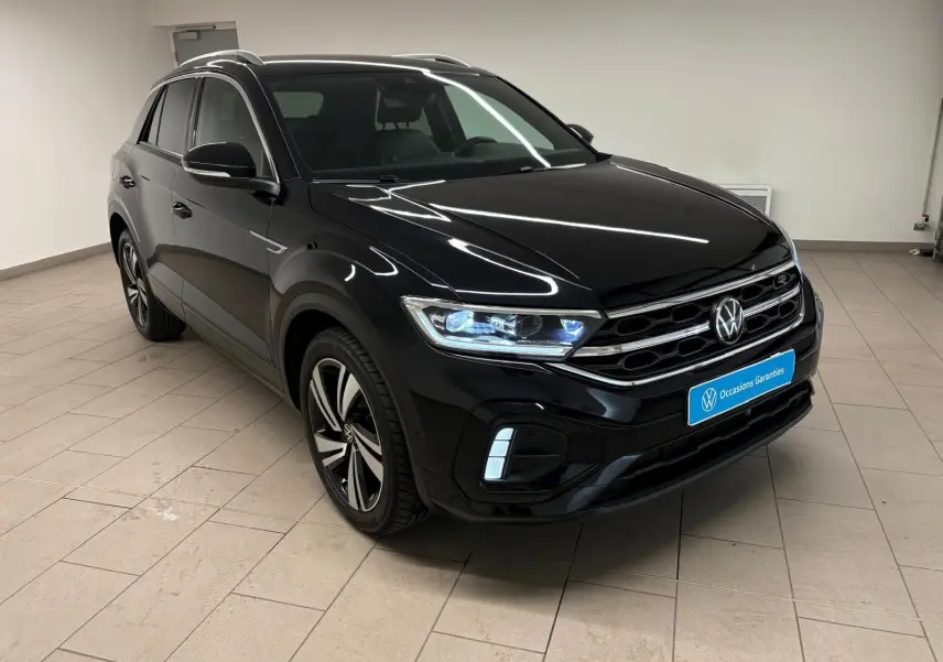 Volkswagen T-Roc noir intense en 3/4 avant droit, avec jantes alliage et phares LED allumés dans un intérieur neutre.
