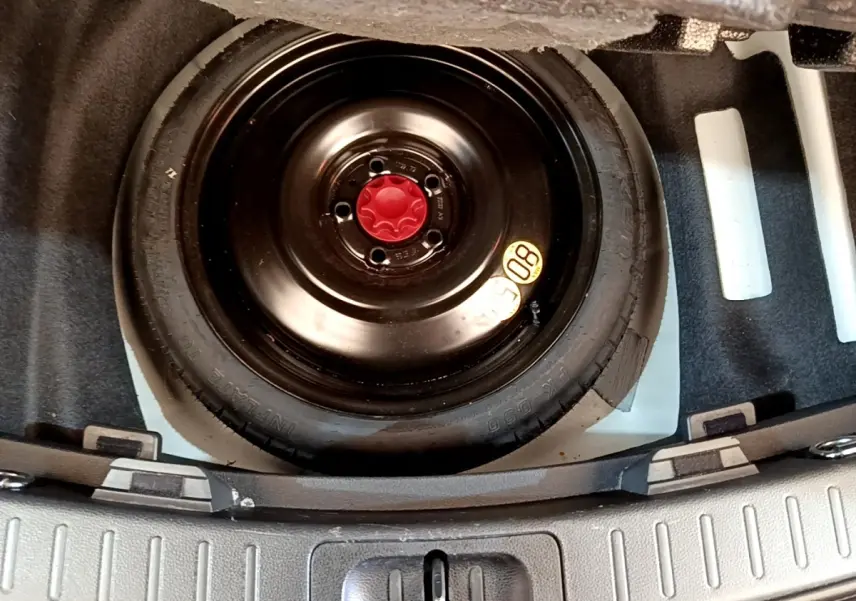 Vue rapprochée de la roue de secours noire avec bouchon rouge dans le coffre d’une Toyota Corolla blanche hybride 2022.