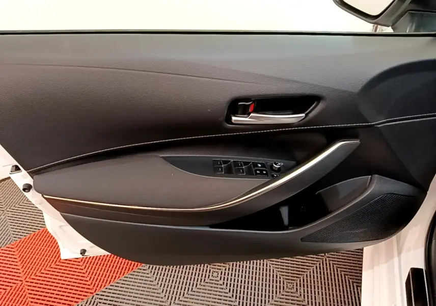 Vue intérieure côté gauche de la porte avant blanche d'une Toyota Corolla hybride avec garniture noire et poignée chromée.