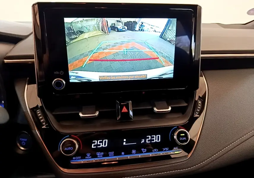 Vue intérieure du tableau de bord de la Toyota Corolla hybride 2022 avec écran de caméra de recul et commandes de climatisation digitales.