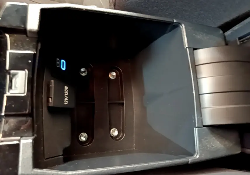 Vue en plongée sur le compartiment de rangement central noir de la Toyota Corolla hybride 2022 avec prise 12V visible.