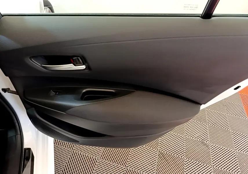 Vue rapprochée de la porte avant gauche noire de la Toyota Corolla hybride blanche, avec poignée argentée et bouton de vitre électrique.