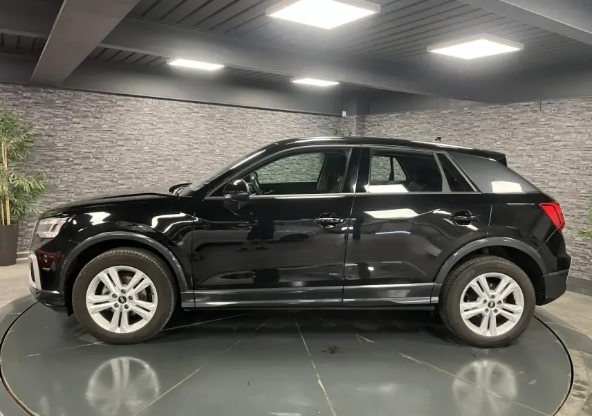 Profil côté gauche d'un Audi Q2 noir brillant 2023 dans un showroom avec jantes aluminium à 5 branches doubles.