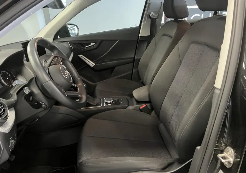 Vue intérieure côté conducteur de l'Audi Q2 2023 noire, montrant sièges tissu et volant multifonction cuir.