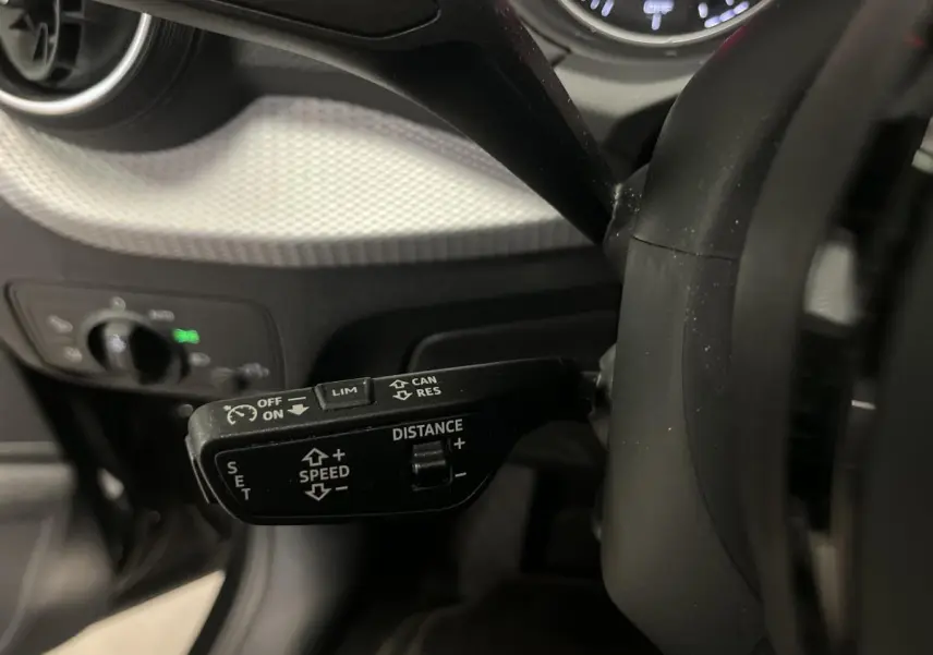 Gros plan sur la commande du régulateur adaptatif à gauche du volant d’un Audi Q2 noir 2023 Design.