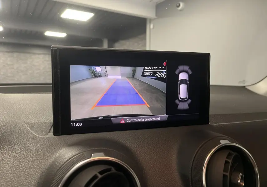 Écran central affichant la caméra de recul et l'aide au stationnement sur le tableau de bord noir de l'Audi Q2 2023