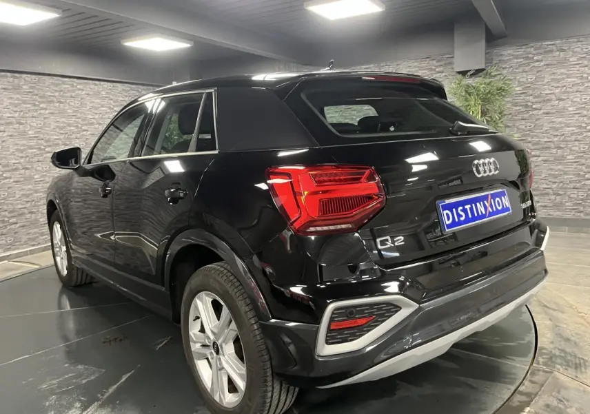 Audi Q2 noir brillant vue 3/4 arrière droit en intérieur avec feux arrière LED et jantes 17 pouces.