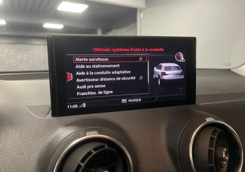 Écran central de l'Audi Q2 2023 affichant les aides à la conduite avec vue du tableau de bord noir.