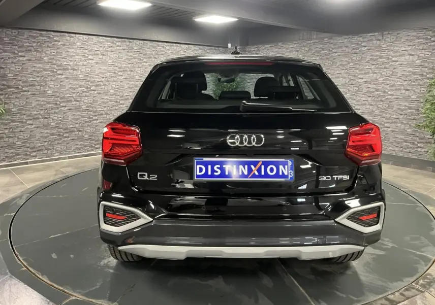 Vue arrière d'un Audi Q2 noir brillant 2023 avec feux LED et logo distinctif sur fond intérieur gris.