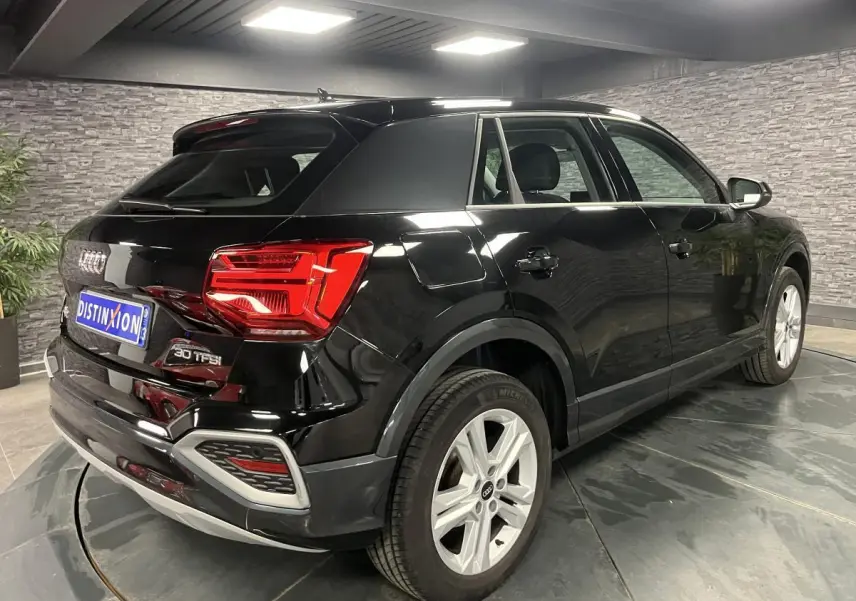 Audi Q2 noir brillant vue 3/4 arrière droit en intérieur avec jantes aluminium 5 branches doubles.