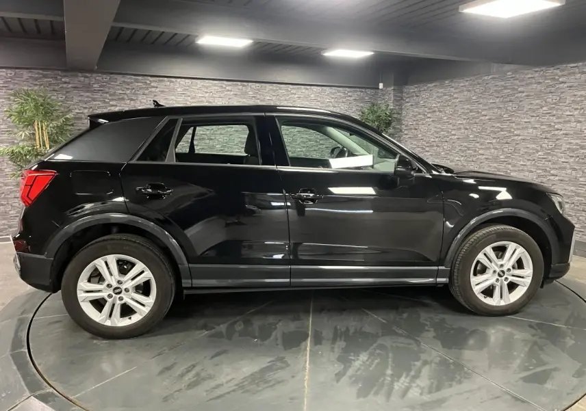 Audi Q2 noir brillant vue de profil côté gauche dans un showroom avec jantes aluminium à 5 branches doubles.