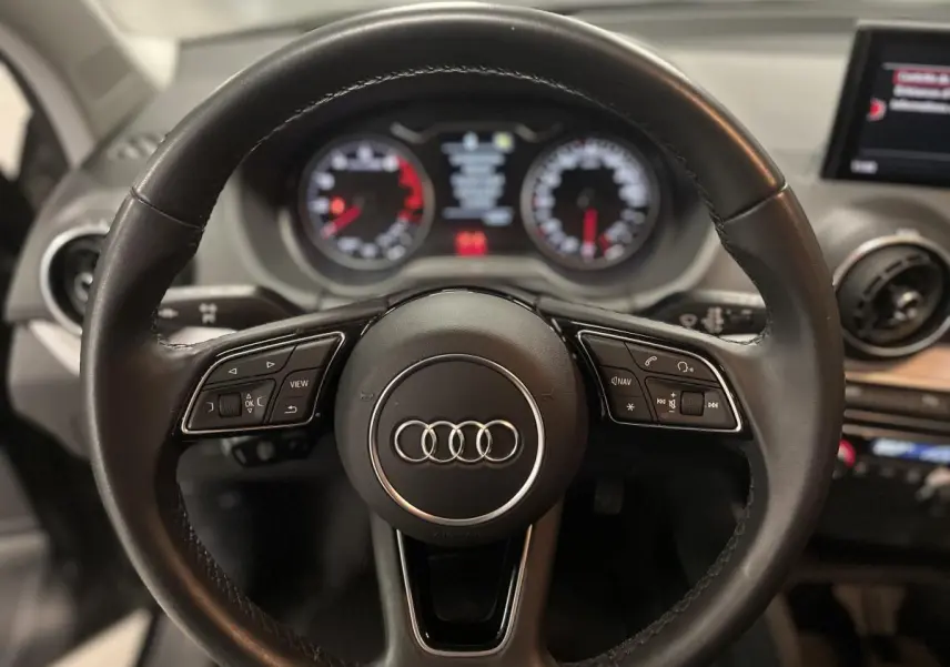 Vue intérieure centrée sur le volant cuir multifonction de l'Audi Q2 1.0 30 TFSI Design 2023 noire, avec aérateurs ronds et écran MMI.