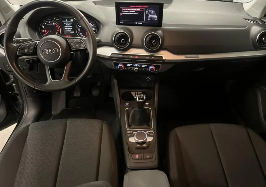 Vue intérieure avant de l'Audi Q2 2023 essence noire, volant cuir, tableau de bord moderne et boîte manuelle.