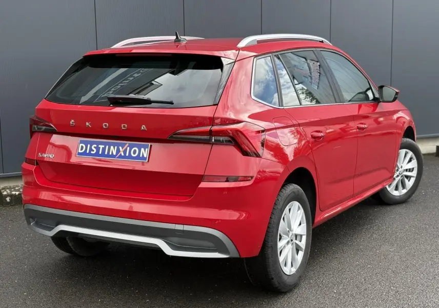 Vue 3/4 arrière droite d'un Skoda Kamiq rouge Velvet avec jantes alliage et barres de toit argentées.