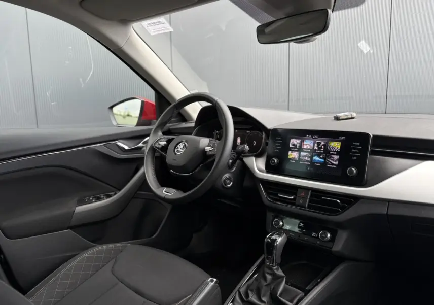 Intérieur du Skoda Kamiq rouge Velvet, vue côté conducteur sur le volant cuir, écran tactile et tableau de bord digital.