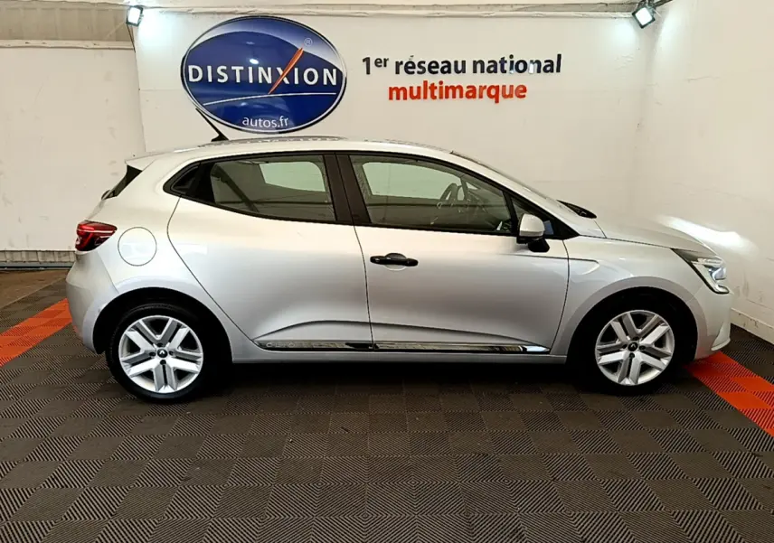 Profil côté gauche d'une Renault Clio Business TCe 100 gris clair, garée en intérieur sur sol à damier noir et rouge.