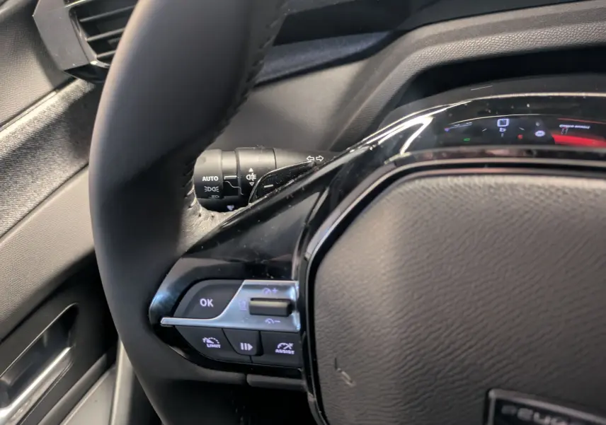 Gros plan sur le volant noir du Peugeot 308 2025, avec commandes intégrées et tableau de bord partiellement visible.