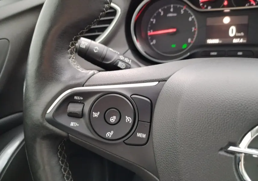 Gros plan sur le volant cuir noir de l'Opel Grandland X gris platinium, avec commandes de régulateur et tableau de bord partiel.