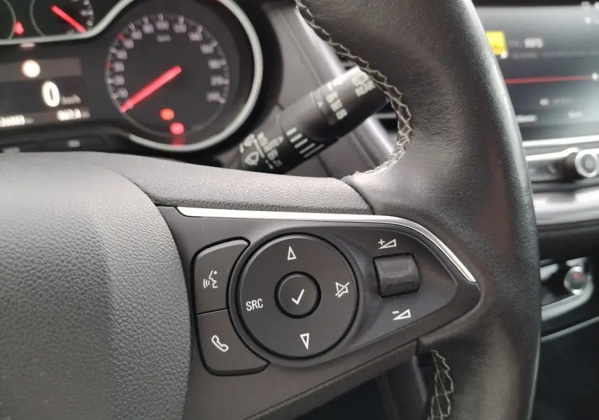 Gros plan sur le volant en cuir noir de l'Opel Grandland X 2019, avec commandes audio et tableau de bord en arrière-plan.