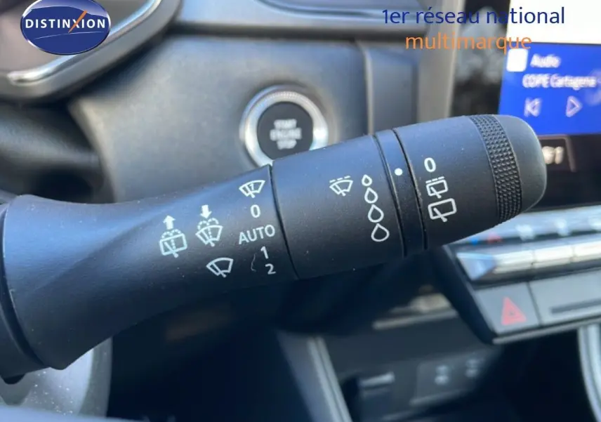 Gros plan sur la commande d’essuie-glace à gauche du volant dans l’habitacle d’un Renault Captur rouge désir métal avec toit noir.