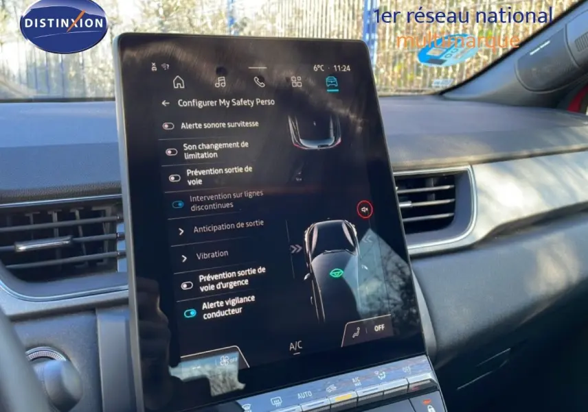 Vue intérieure centrée sur l'écran tactile du tableau de bord du Renault Captur rouge désir métal avec toit noir, affichant les aides à la conduite.