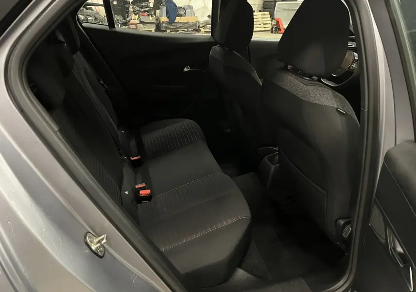 Vue intérieure côté arrière droit du Peugeot 2008 gris alu, montrant les sièges arrière en tissu noir et l'avant du véhicule.