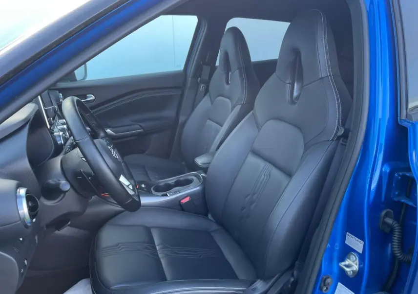 Vue intérieure côté conducteur du Nissan Juke 2024 bleu magnetic, sièges avant en TEP noir avec surpiqûres blanches.