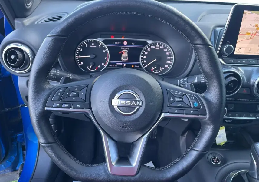 Vue rapprochée du volant en cuir noir du Nissan Juke 2024 bleu magnetic avec tableau de bord digital et écran tactile.