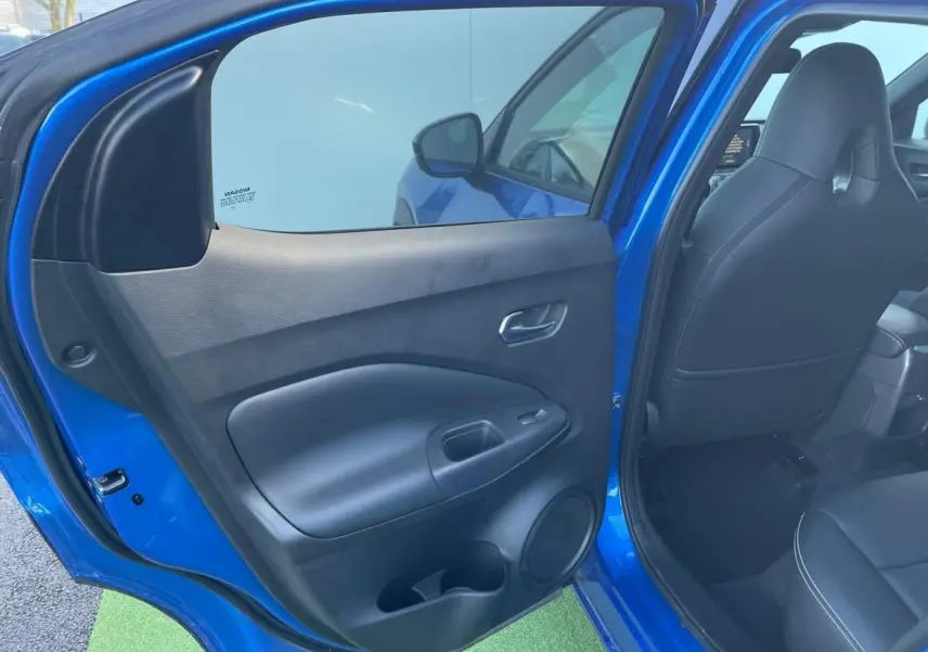 Vue intérieure côté gauche de la porte arrière ouverte d'un Nissan Juke II bleu magnetic, avec siège noir visible.
