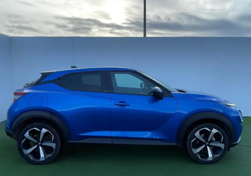 Profil droit du Nissan Juke II 2024 en bleu magnetic avec jantes alliage noires et vitres teintées.