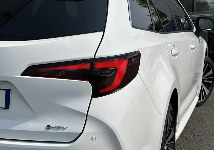 Vue 3/4 arrière droite de la Toyota Corolla Touring Sport blanche Neige avec feux arrière LED et jantes alliage noires.