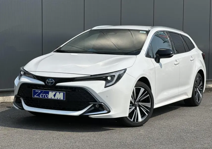 Toyota Corolla Touring Sport blanc neige vue 3/4 avant droit avec jantes alliage et calandre noire sportive.