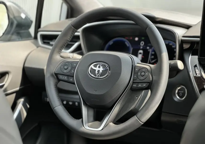 Volant multifonction noir de Toyota Corolla Touring Sport 2025, avec tableau de bord numérique et bouton démarrage visible.