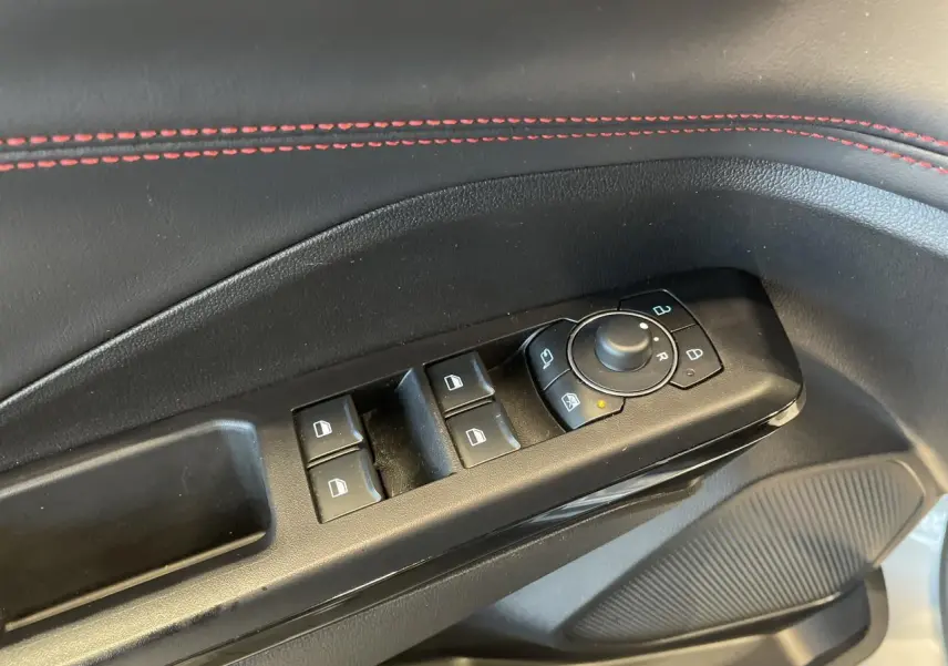 Gros plan sur la commande des vitres et rétroviseurs côté conducteur, avec surpiqûres rouges sur la garniture noire.