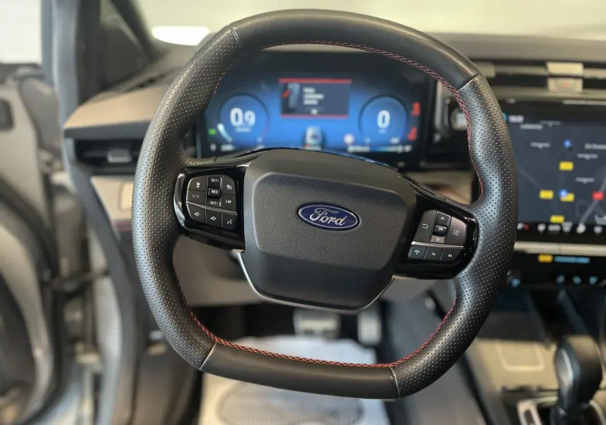 Volant en cuir noir avec surpiqûres rouges du Ford Puma 2024, tableau de bord numérique et écran tactile visibles en arrière-plan.