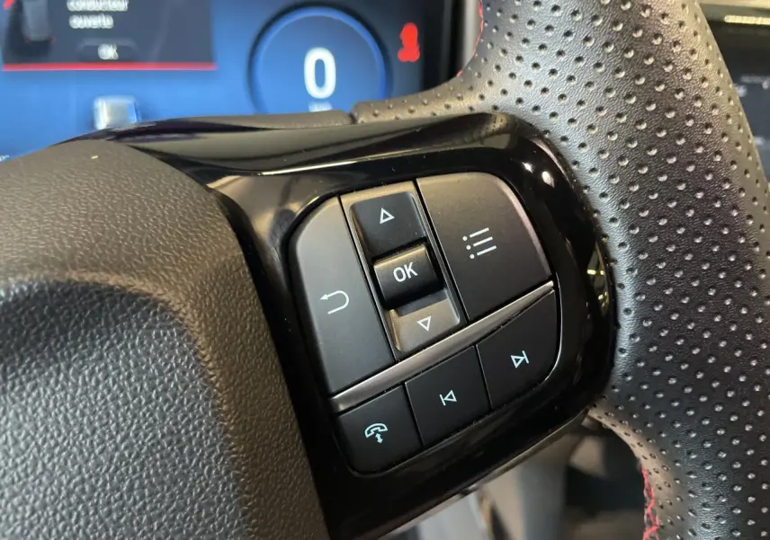 Gros plan sur les commandes multifonctions noires du volant perforé du Ford Puma gris clair 2024.