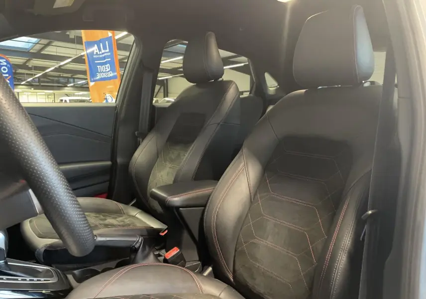 Vue intérieure du côté conducteur du Ford Puma 2024, sièges noirs en suédine et cuir avec surpiqûres rouges visibles.