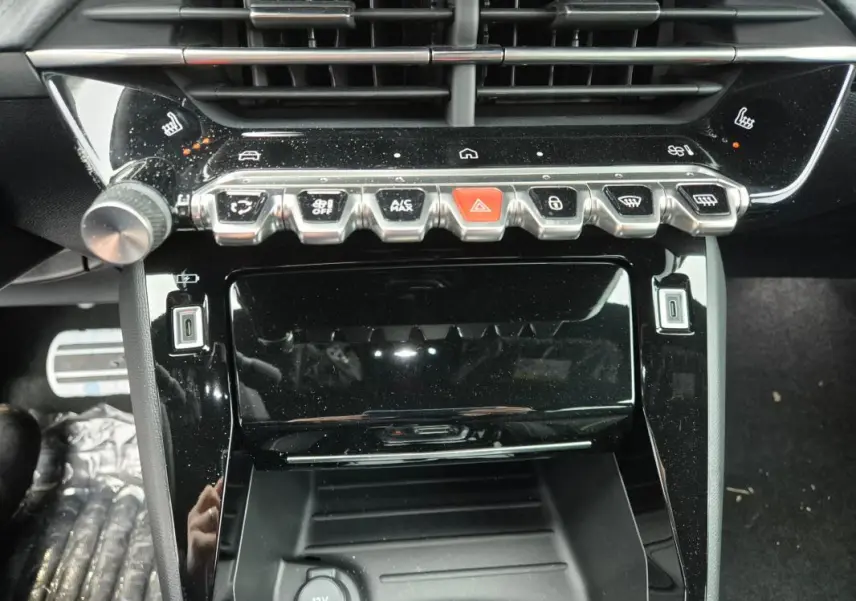 Gros plan sur la console centrale noire brillante du Peugeot 208 Hybrid 110 e-DCS6 GT avec boutons de commande et prise USB visibles.