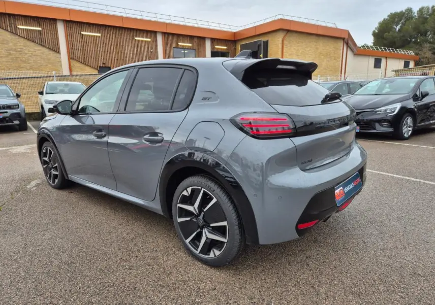 Peugeot 208 Hybrid 110 GT gris vue 3/4 arrière droit, jantes alliage 17 pouces et feux arrière LED allumés.