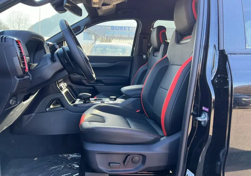 Vue intérieure côté conducteur du Ford Ranger Raptor noir absolu 2025, sièges sport noirs avec surpiqûres rouges et volant cuir multifonctions.