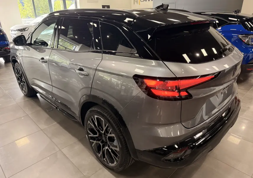 Vue 3/4 arrière droite du Renault Austral gris schiste avec toit noir et feux arrière allumés en intérieur showroom.