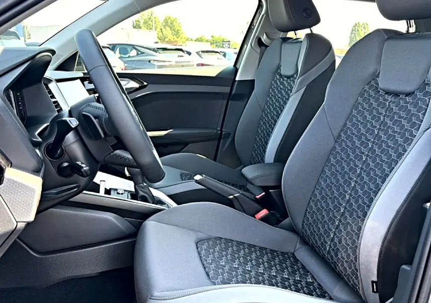 Vue intérieure côté conducteur de l’Audi A1 Sportback 2026, sièges sport gris avec motifs hexagonaux et volant cuir multifonction.